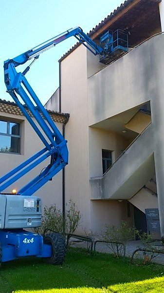 Nacelle élévatrice articulée 4x4 déployée le long d'une façade, panier positionné au niveau de la rive de toiture